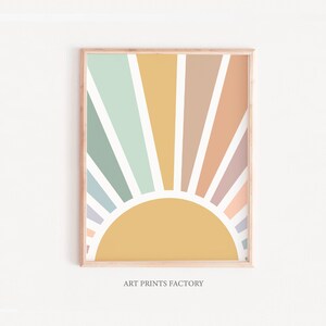 May include: A framed print of a colourful abstract sunburst design with a yellow sun in the centre. The sunburst is made up of pastel colours, including light blue, green, pink, and orange. The print is framed in a light wood frame.