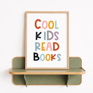 May include: A rectangular wooden frame containing a white print with the multicolored text COOL KIDS READ BOOKS. The letters are displayed in various colors including orange, pink, yellow, blue, grey, purple, and black, set against a white background.