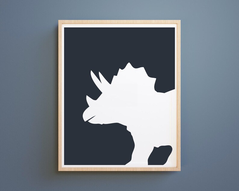 May include: A white silhouette of a triceratops dinosaur on a dark blue background. The image is framed in a light wood frame.