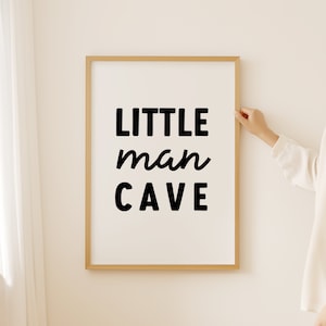Op de afbeelding: Een ingelijst print met de tekst "LITTLE man CAVE" in zwarte letters op een witte achtergrond.