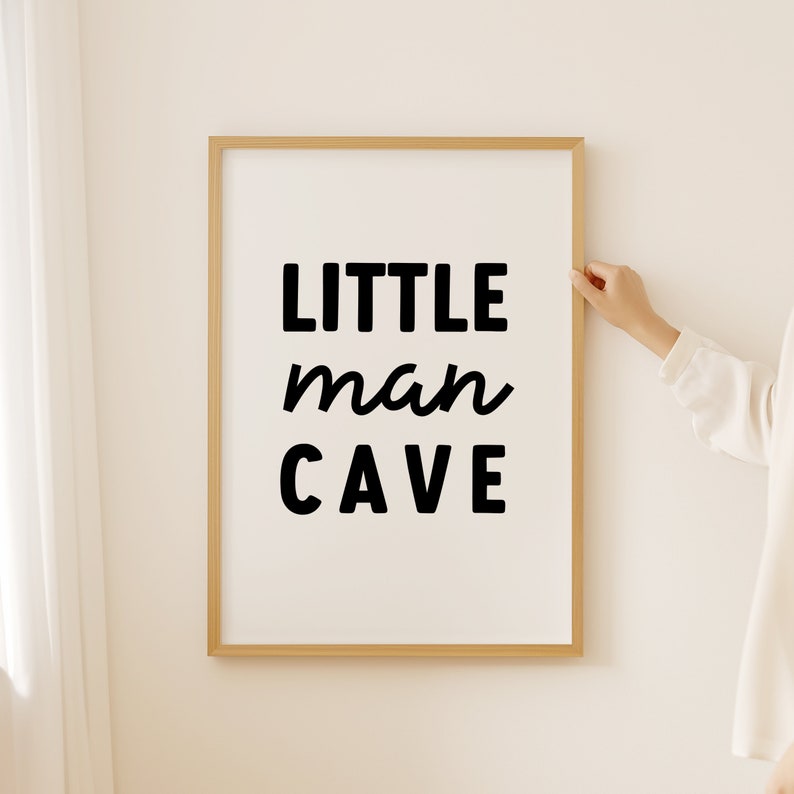 Op de afbeelding: Een ingelijst print met de tekst "LITTLE man CAVE" in zwarte letters op een witte achtergrond.