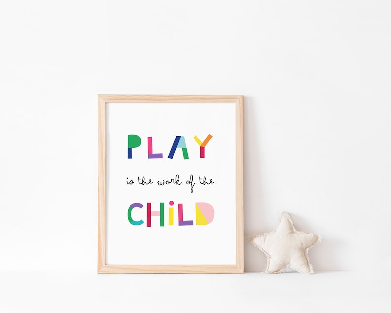 May include: A framed print with the text "PLAY is the work of the CHILD" in colorful, geometric letters. The frame is light wood and the background is white.