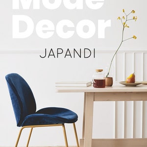 May include: A blue velvet chair with gold legs sits in front of a wooden table with a vase of yellow flowers, a book, and a glass jar with a brown liquid. The text "Mode Decor" and "Japandi" is written on the wall behind the table. The text "Velvet Vibes" is written on the floor in front of the chair.
