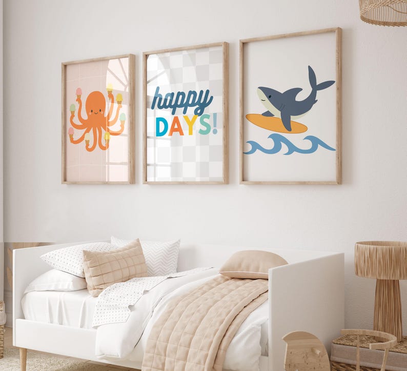 Puede incluir: Tres impresiones art&iacute;sticas enmarcadas con tem&aacute;tica de playa. Una impresi&oacute;n presenta un pulpo naranja sosteniendo conos de helado, otra dice "happy DAYS!", y la &uacute;ltima muestra un tibur&oacute;n surfeando sobre una tabla amarilla sobre olas azules. Las impresiones est&aacute;n en un marco de madera clara.