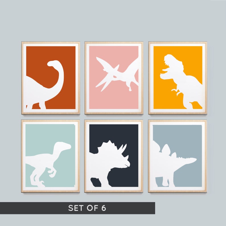 May include: Set of six framed prints featuring white dinosaur silhouettes on colored backgrounds. The prints include a brown background with a Brachiosaurus, a pink background with a Pterodactyl, a yellow background with a Tyrannosaurus Rex, a light blue background with a Velociraptor, a dark blue background with a Triceratops, and a light gray background with a Stegosaurus. The prints are labeled "SET OF 6".