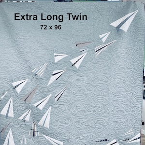 May include: A blue quilted fabric with a white swirl pattern. The fabric is decorated with paper airplanes in various sizes and patterns. The text "Extra Long Twin 72 x 96" is printed in black at the top of the fabric.