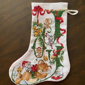 Könnte beinhalten: Ein weißer Weihnachtssocken mit rotem Besatz und einem grünen gestickten Design des Wortes "Freude" mit einem Bären und Mäusen.