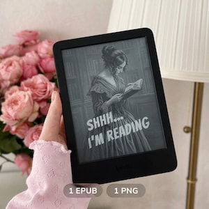 Pode incluir: Leitor de e-books Kindle preto exibindo uma imagem em tons de cinza de uma mulher lendo, com o texto "SHHH... I'M READING". O leitor é segurado em frente a um buquê de rosas cor-de-rosa.