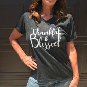 May include: A dark gray V-neck t-shirt with the text "Thankful & Blessed" in white lettering.