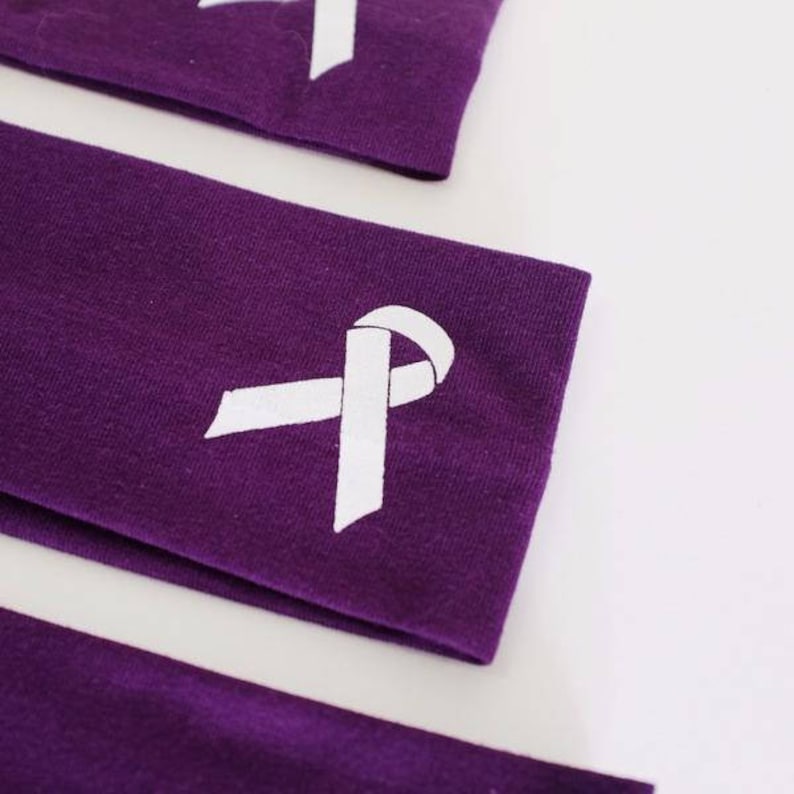 Puede incluir: Tres diademas de tela morada con un dise&ntilde;o de cinta blanca. Las diademas est&aacute;n dobladas y apiladas una encima de la otra.
