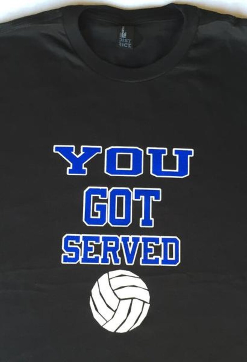 May include: Black t-shirt with the text "YOU GOT SERVED" in blue and white lettering, along with a white volleyball graphic. The shirt is a casual wear item, perfect for sports enthusiasts.