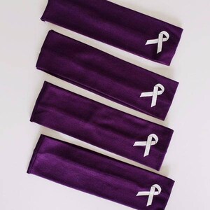 Puede incluir: Cinco diademas de tela morada con un dise&ntilde;o de cinta blanca. Las diademas est&aacute;n apiladas, con la diadema superior mostrando el dise&ntilde;o de la cinta.