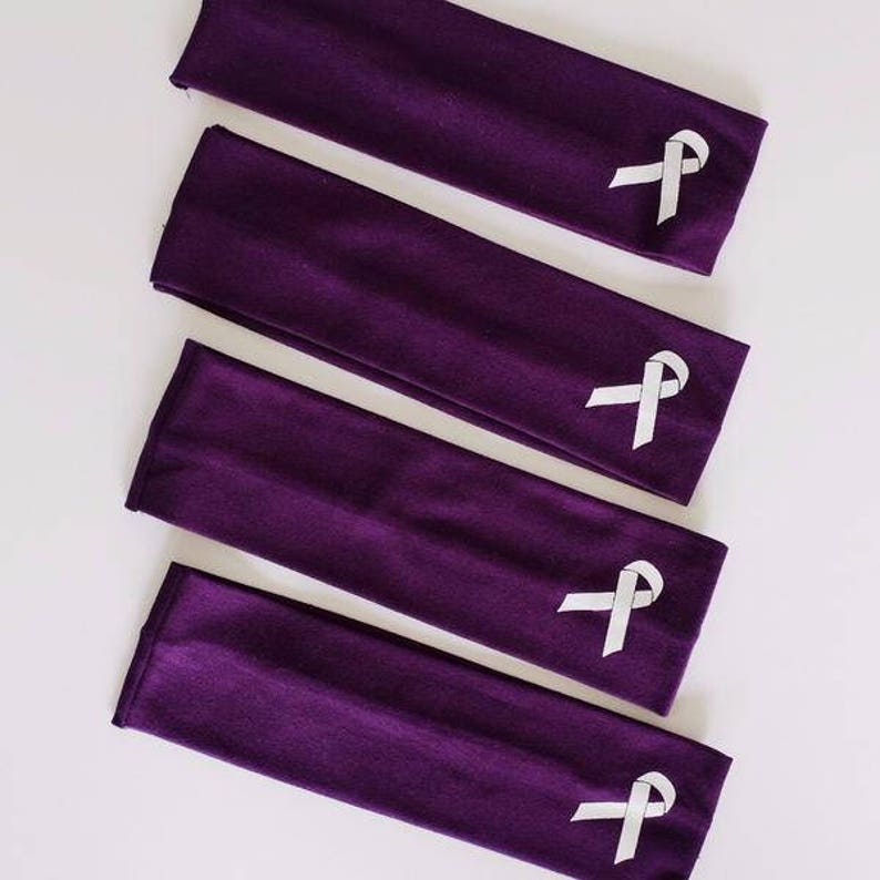 Puede incluir: Cinco diademas de tela morada con un dise&ntilde;o de cinta blanca. Las diademas est&aacute;n apiladas, con la diadema superior mostrando el dise&ntilde;o de la cinta.
