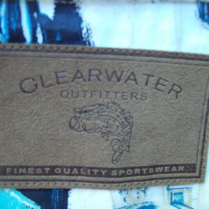 May include: A brown leather patch with the text "Clearwater Outfitters" and "Finest Quality Sportswear". A stylized fish illustration is below the text.