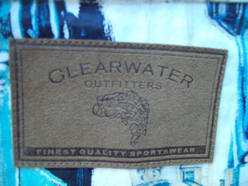 May include: A brown leather patch with the text "Clearwater Outfitters" and "Finest Quality Sportswear". A stylized fish illustration is below the text.