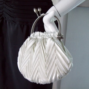 May include: A white satin clutch bag with a pleated design and a silver clasp.