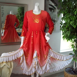 May include: A vibrant red dress with long sleeves and gold embellishments. The dress features a flowing skirt with white and gold ruffled trim. The dress is displayed on a mannequin, showcasing its design and details.