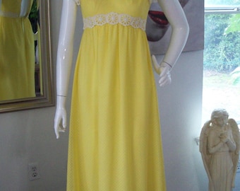 May include: A yellow vintage dress with white lace trim and a floral pattern. The dress is sleeveless and has a high neckline with white lace trim. The dress is displayed on a mannequin.