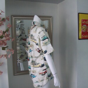May include: A white button-down shirt with a colorful print of vintage cars. The shirt has short sleeves and a relaxed fit.
