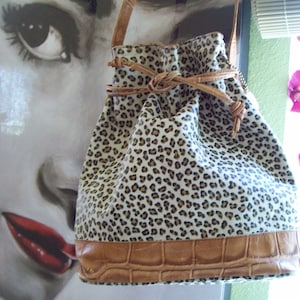 May include: A white and brown leopard print drawstring bag with a brown leather bottom and a brown leather strap.