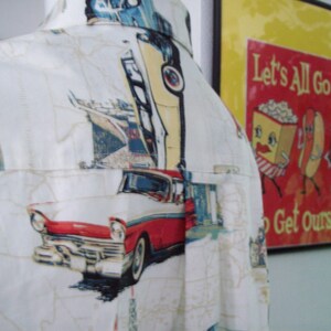 May include: A white button-down shirt with a vintage car and other graphic prints. The shirt has a pocket on the left side and a collar. The shirt is made of a lightweight fabric and is perfect for warm weather.