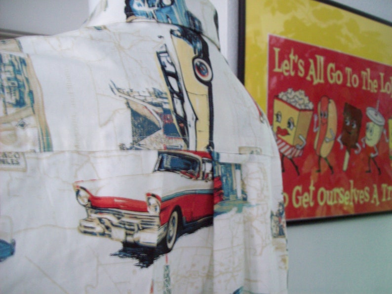 May include: A white button-down shirt with a vintage car and other graphic prints. The shirt has a pocket on the left side and a collar. The shirt is made of a lightweight fabric and is perfect for warm weather.