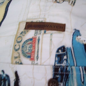 May include: White button-up shirt with a brown leather patch that says "The Navigator". The shirt has a blue and white pattern of cars and the text "El Conquistador" on the left side.