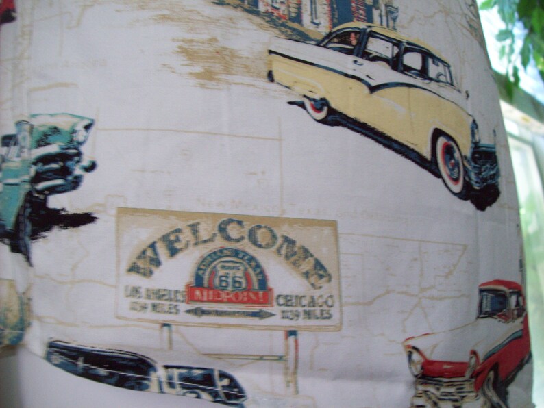 May include: A white fabric with a vintage Americana theme. The fabric features a welcome sign with Route 66, a classic car, and a map. The text on the sign reads "Welcome, Los Angeles 1539 Miles, Chicago 1539 Miles, Route 66, Midpoint!"