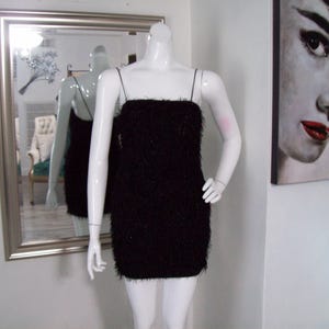 May include: A black mini dress with a fuzzy texture. The dress has thin straps and a straight neckline.