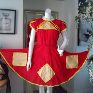May include: A vintage red dress with yellow and tan accents. The dress features a round neckline, short sleeves, and a flared skirt with three tan square patches. The edges are trimmed with yellow zigzag stitching. The dress is displayed on a mannequin.