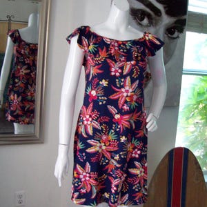 May include: A navy blue dress with a vibrant floral pattern in shades of pink, orange, and yellow. The dress features a ruffled neckline and short sleeves. The dress is displayed on a mannequin.