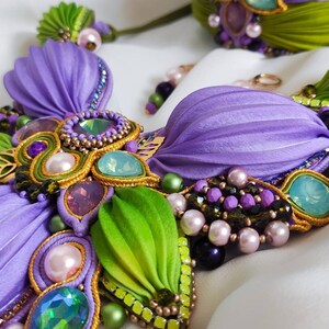 May include: A purple and green beaded necklace with iridescent gemstones and pearls. The necklace is made with fabric flowers and gold trim.