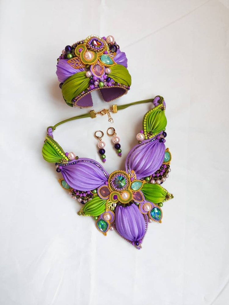 May include: A purple and green jewelry set with a necklace, bracelet, and earrings. The necklace and bracelet feature a floral design with intricate details and colorful beads. The earrings are simple and elegant.