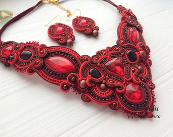 May include: A red and brown beaded necklace and earrings set with large red crystal accents. The necklace is a statement piece with a unique, intricate design.
