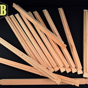 May include: A pile of wooden beehive frames, made of unfinished light brown wood. The frames are designed to hold honeycomb.