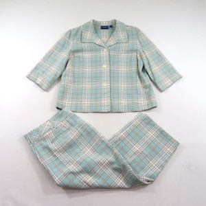 Puede incluir: Un conjunto de dos piezas que consta de una chaqueta abotonada y pantalones a juego. La chaqueta presenta mangas de tres cuartos, cuello con solapa y tres botones frontales. Ambas piezas están confeccionadas en tela de cuadros azul claro y blanco.