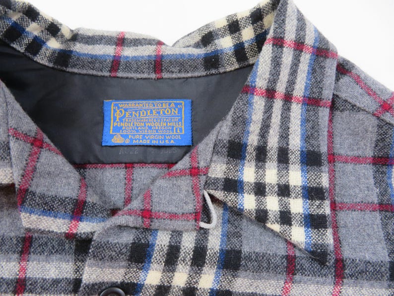 May include: A gray plaid shirt with a collar and a blue Pendleton label sewn into the inner neckline. The label reads Warranted to be a Pendleton, Pendleton Woolen Mills, Portland, Oregon, 100% Virgin Wool, Size L, Pure Virgin Wool, Made in U.S.A.