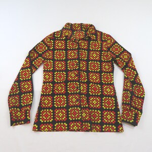 May include: A long-sleeved button-down shirt featuring a repeating geometric pattern of red and yellow square motifs on a black background. The shirt has a pointed collar, a front button placket, and cuffs at the end of each long sleeve.