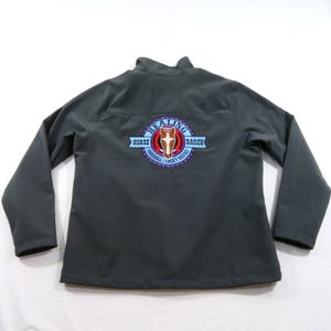 May include: A dark gray long-sleeve jacket featuring a circular logo on the back. The logo displays a brown horse head graphic, the text HEALING HORSE RANCH, and the words PARSHALL / LUCKY MOUND on a light blue banner against a dark background.