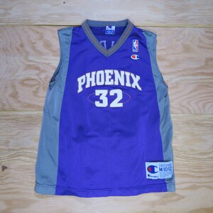 May include: Purple and gray Phoenix Suns basketball jersey. The sleeveless jersey features the word "PHOENIX" in white block letters and the number "32". A Champion and NBA logo are visible.