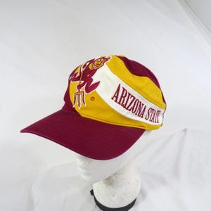 May include: A maroon and gold baseball cap featuring an embroidered maroon devil mascot holding a trident and the text ARIZONA STATE printed in maroon on a white diagonal stripe across the front panels of the hat with a solid maroon brim.