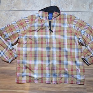 May include: A tan, red, and white plaid jacket with a black collar and a full-length zip. The jacket features long sleeves and a classic plaid pattern. The jacket is laid flat on a tiled surface.