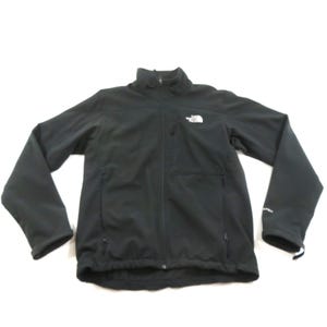 Può includere: Una giacca nera a maniche lunghe con collo alto e chiusura frontale a zip. Il capo presenta due tasche laterali con zip, una tasca sul petto con zip e il logo bianco The North Face posizionato sul petto a sinistra e sulla manica sinistra.