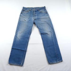 May include: A pair of light blue denim jeans featuring a classic five-pocket design, a button fly closure, and a faded wash finish. The jeans have a straight-leg cut with visible whiskering and a small dark mark on the upper right thigh area.