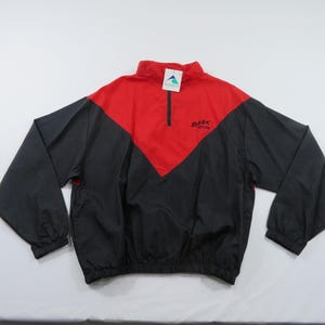 Puede incluir: Chaqueta cortavientos roja y negra con cierre de media cremallera. La chaqueta presenta una sección superior roja y una sección inferior negra con mangas largas. El texto "DARE" está impreso en la sección roja.