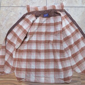 May include: Open brown and white plaid flannel shirt with a quilted brown lining. The shirt has a button-down front and a classic collar. The interior features a plaid pattern in shades of brown and white.