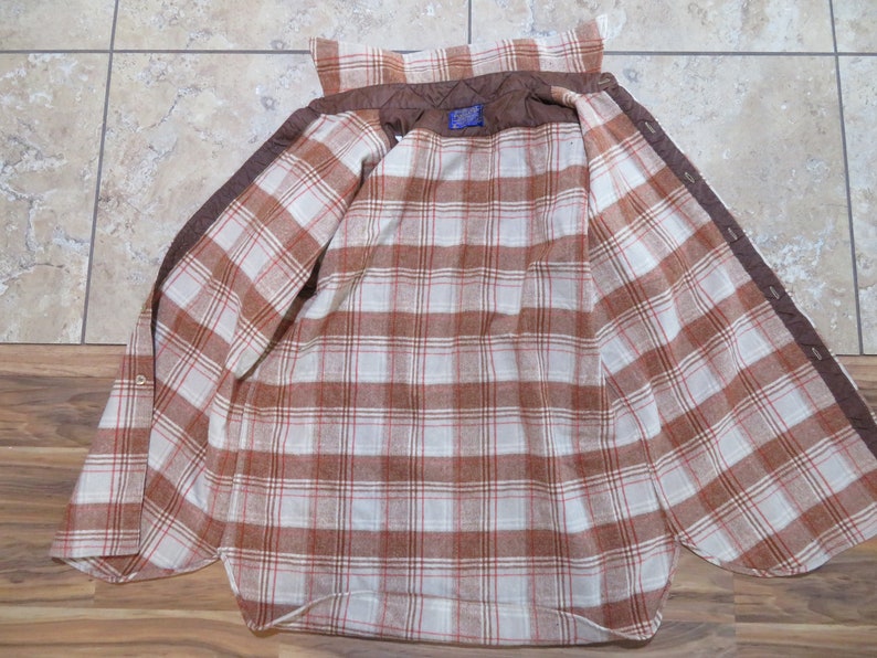 May include: Open brown and white plaid flannel shirt with a quilted brown lining. The shirt has a button-down front and a classic collar. The interior features a plaid pattern in shades of brown and white.