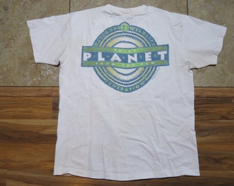 May include: White t-shirt with a circular graphic on the back. The graphic features the text "NATIONAL WILDLIFE FEDERATION" around the top, and "THIRD PLANET FROM THE SUN" in a rectangular box. The shirt is made of a soft material.