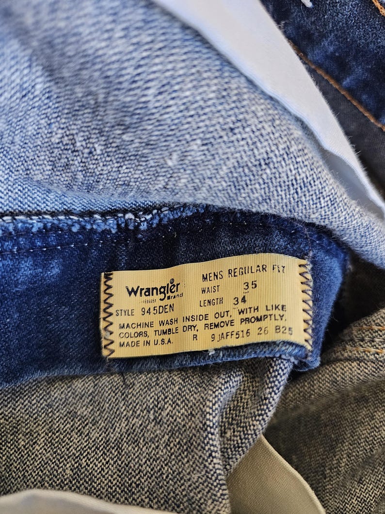 May include: Close-up of a pair of blue denim jeans. The jeans have a label that reads "Wrangler" and includes the waist size 35 and length 34. The label also provides washing instructions. Made in the U.S.A.