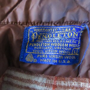 May include: Close-up of a blue Pendleton label with gold lettering, stitched onto a brown quilted fabric. The label reads "Pendleton Woolen Mills, Portland, Oregon, 100% Virgin Wool, Made in U.S.A."